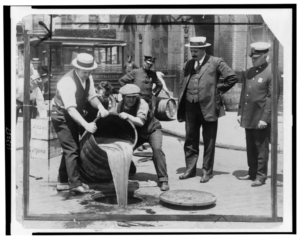 New York City Deputy Police Commissioner John A. Leach, right, watching agents pour alcohol into sewer following a raid during the height of prohibition